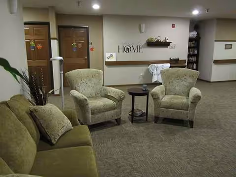 A cozy lounge area with beige chairs, sofas, and small tables in a senior living facility.