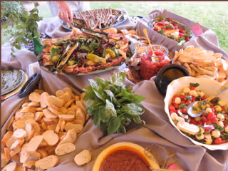A buffet table with assorted appetizers and salads including sliced bread, crostini, chips, dips, and fresh herbs.