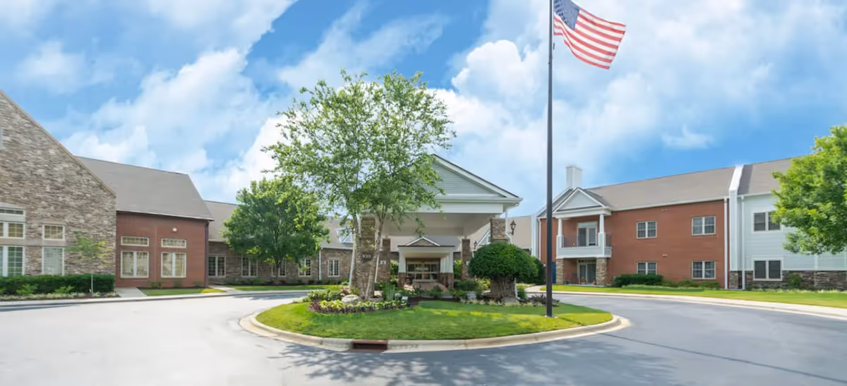 Front entrance of Pennybyrn at Maryfield with a circular driveway, landscaped island, and an American flag.