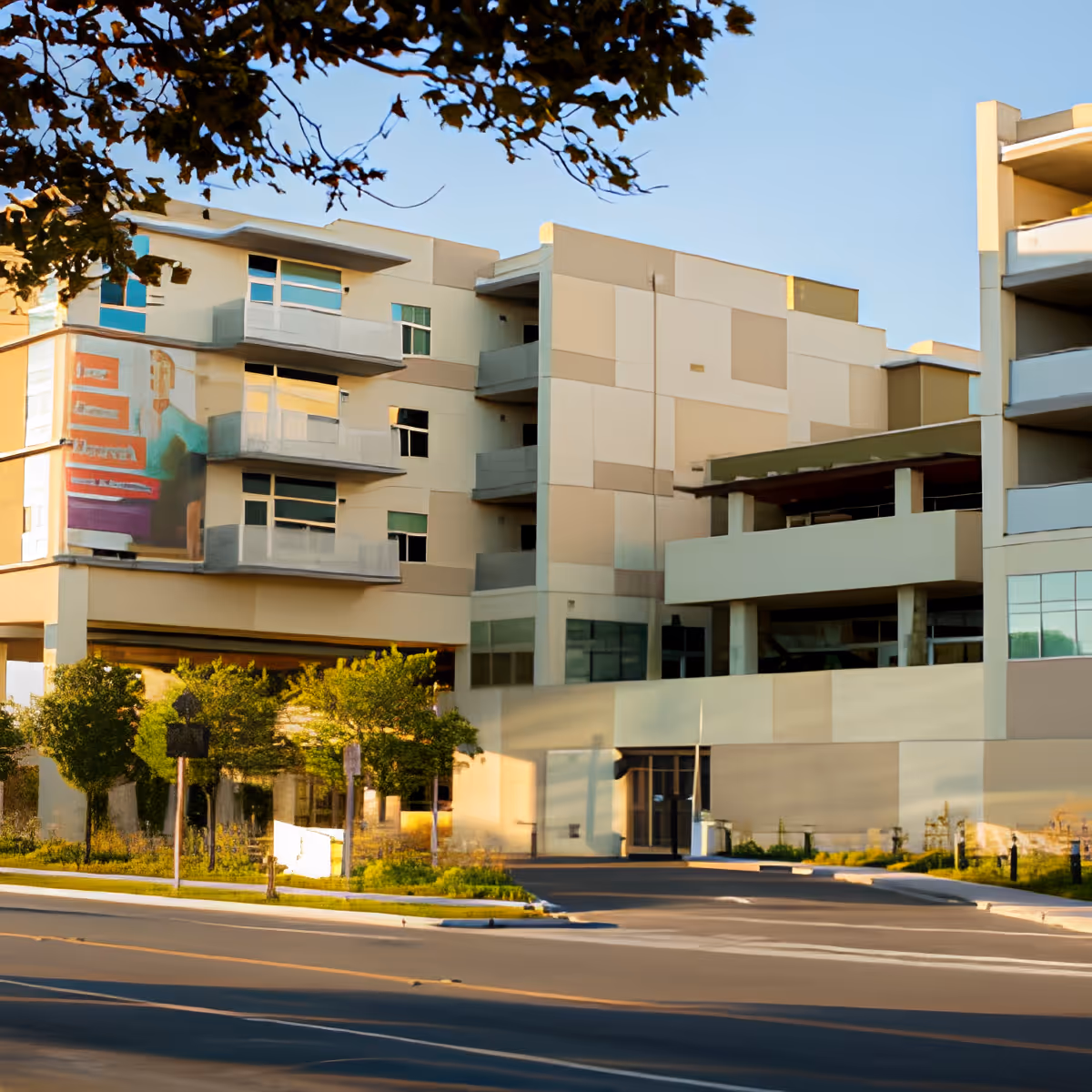 Exterior view of Moldaw Residences, a modern multi-story building with balconies and large windows, surrounded by trees and greenery under a clear blue sky.