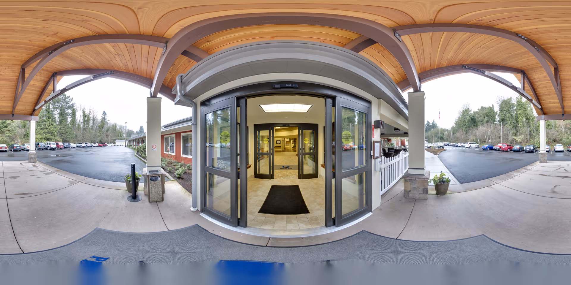 Covered porte-cochere with a curved wooden ceiling leading to automatic glass entry doors and a view of the parking lot on both sides.