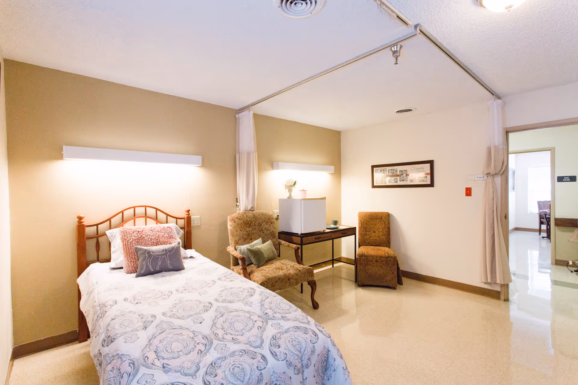 Furnished senior bedroom with a single bed, two armchairs, a small table and soft neutral decor.