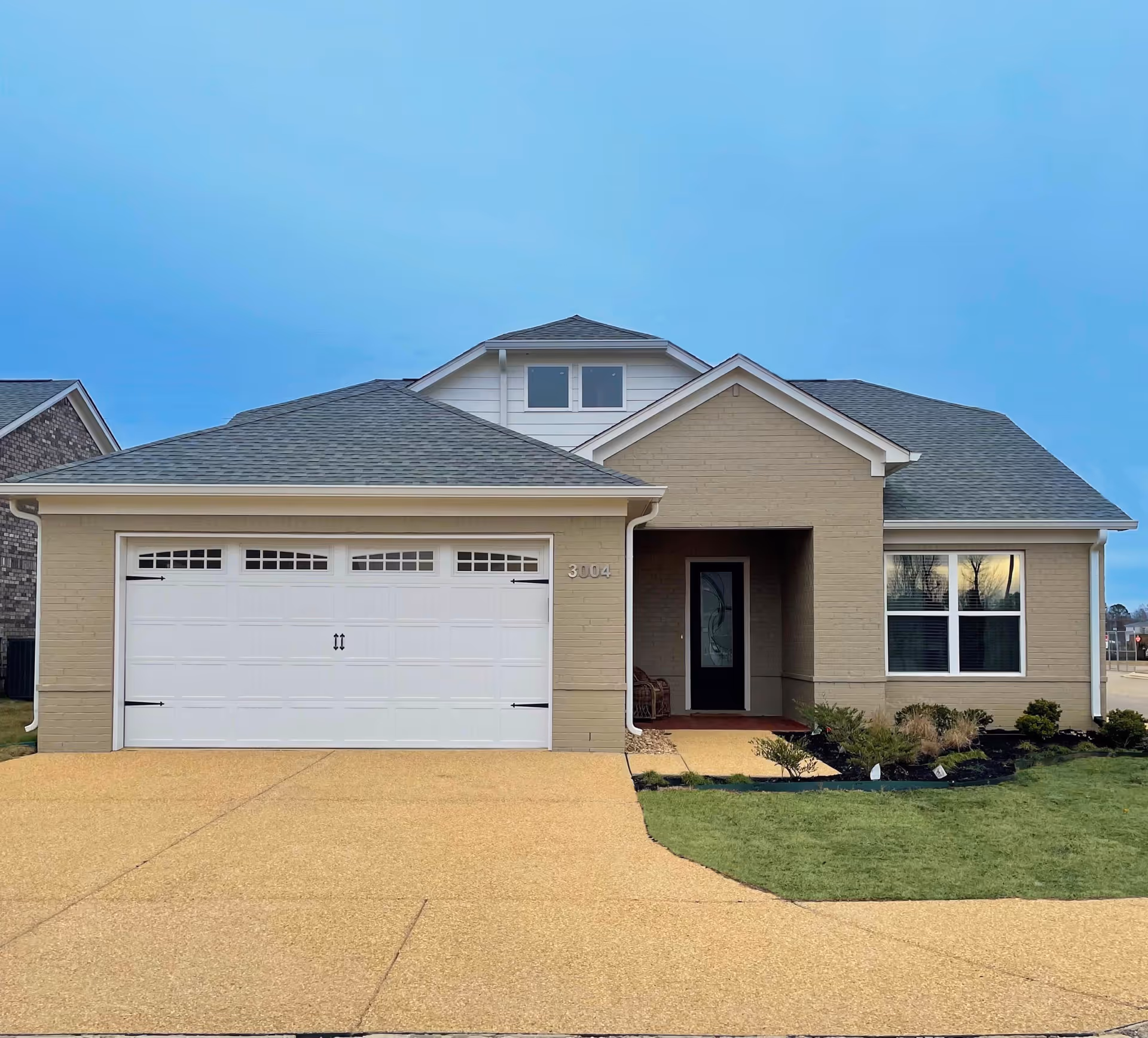 Front exterior of a single-story suburban house with an attached two-car garage, driveway, and small landscaped front lawn.