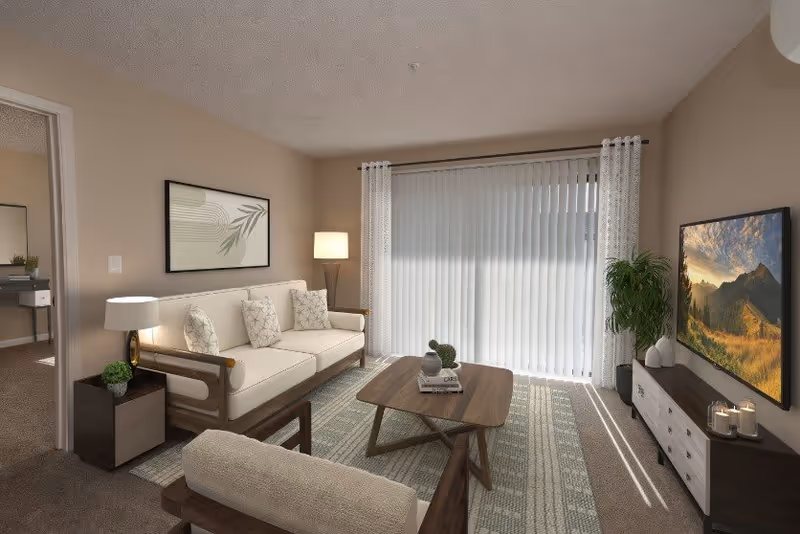A cozy living room with a beige sofa and armchair, a wooden coffee table with decorative items, a floor lamp, a side table with a lamp and plant, a large window with vertical blinds and sheer curtains, a TV on a stand displaying a mountain landscape, and a potted plant next to the TV stand.