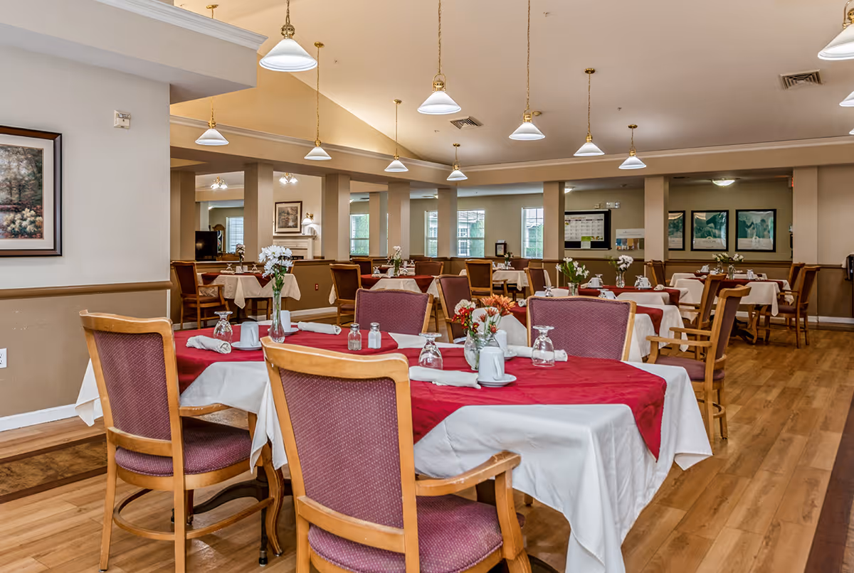 Dining room with tables set with red and white tablecloths, wooden chairs, hanging pendant lights, and floral centerpieces.