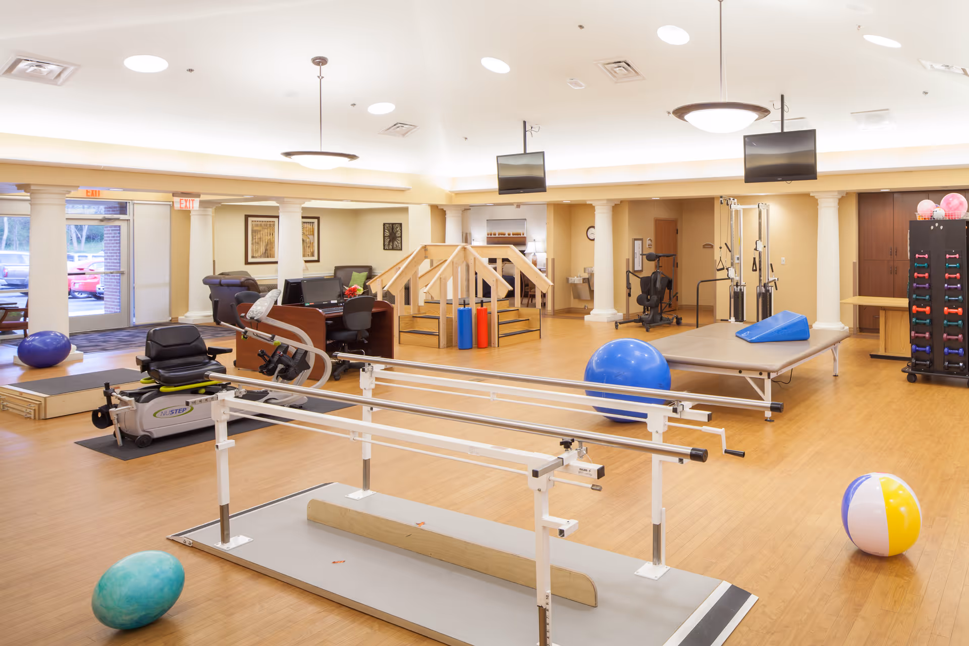 Spacious indoor rehabilitation/therapy room with parallel bars, exercise balls, therapy stairs, and various exercise equipment.