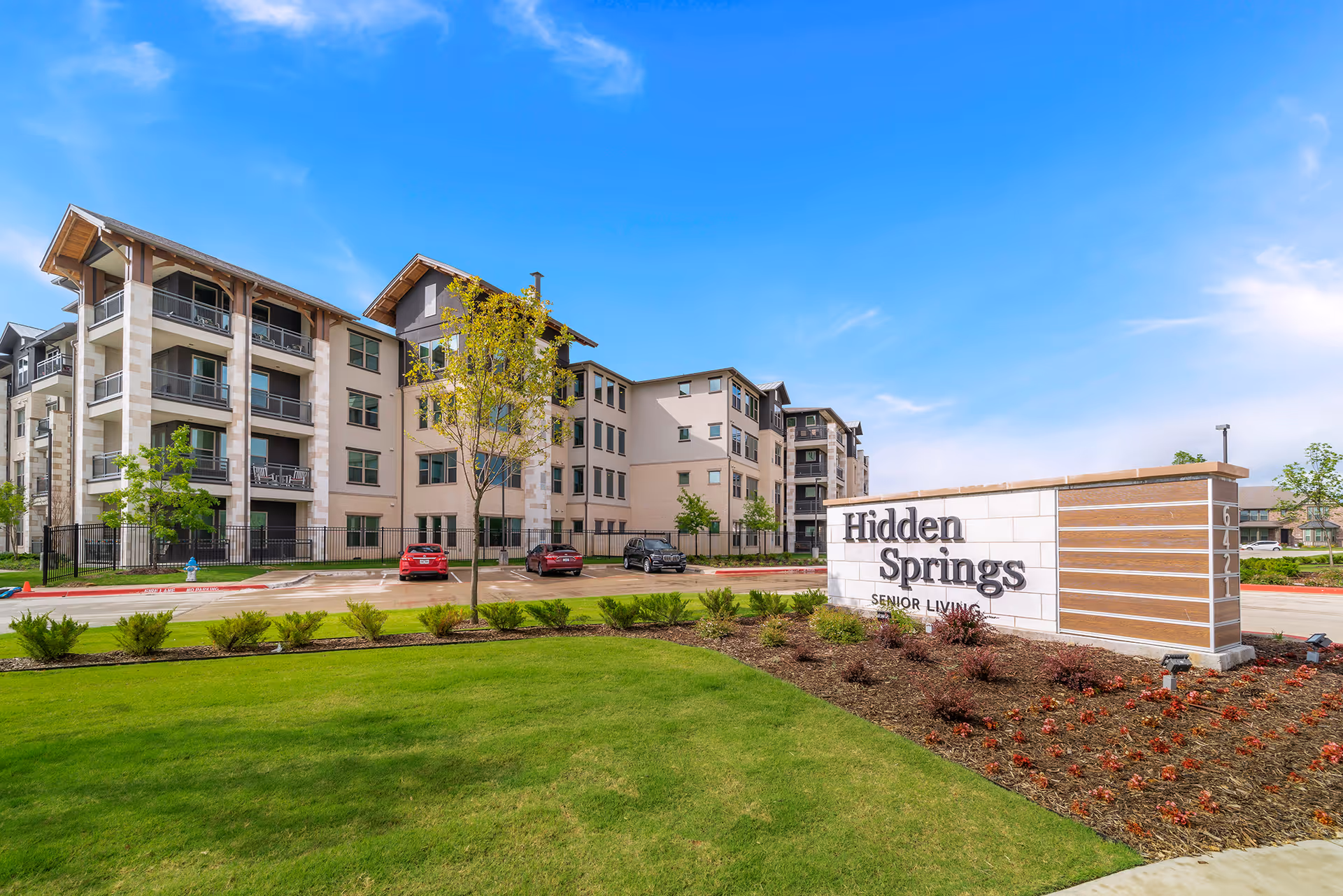 Exterior view of the Hidden Springs senior living building with landscaped lawn and a large entrance sign in front.