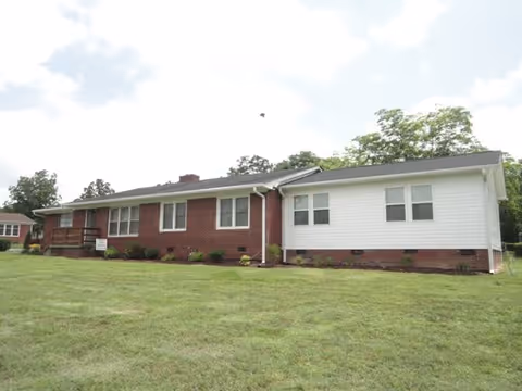 Single-story brick and white-siding building with multiple windows and a large grassy lawn in front.