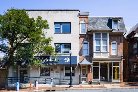 Exterior street view of a mixed brick and stucco building with storefronts and a tree.