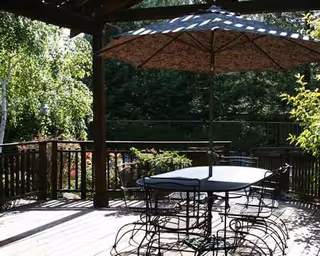 Outdoor wooden deck at Golden Pond with metal table, chairs, and a large umbrella.