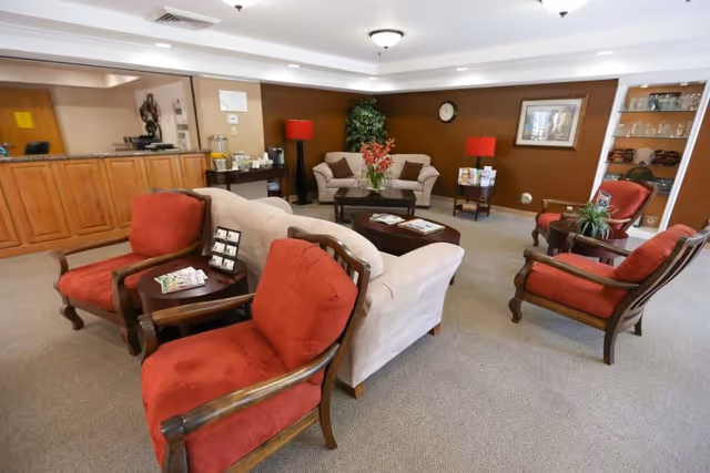 Cozy common room with sofas, red upholstered armchairs, coffee tables, and a reception desk in the background.