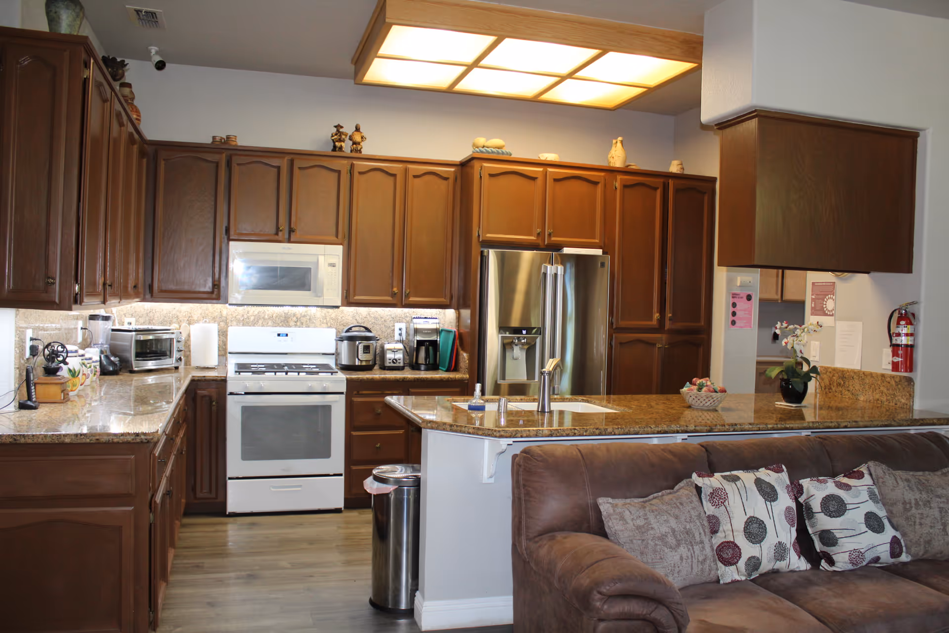 Open kitchen with wooden cabinets, granite countertops, a white stove and stainless refrigerator, and a couch in the foreground.