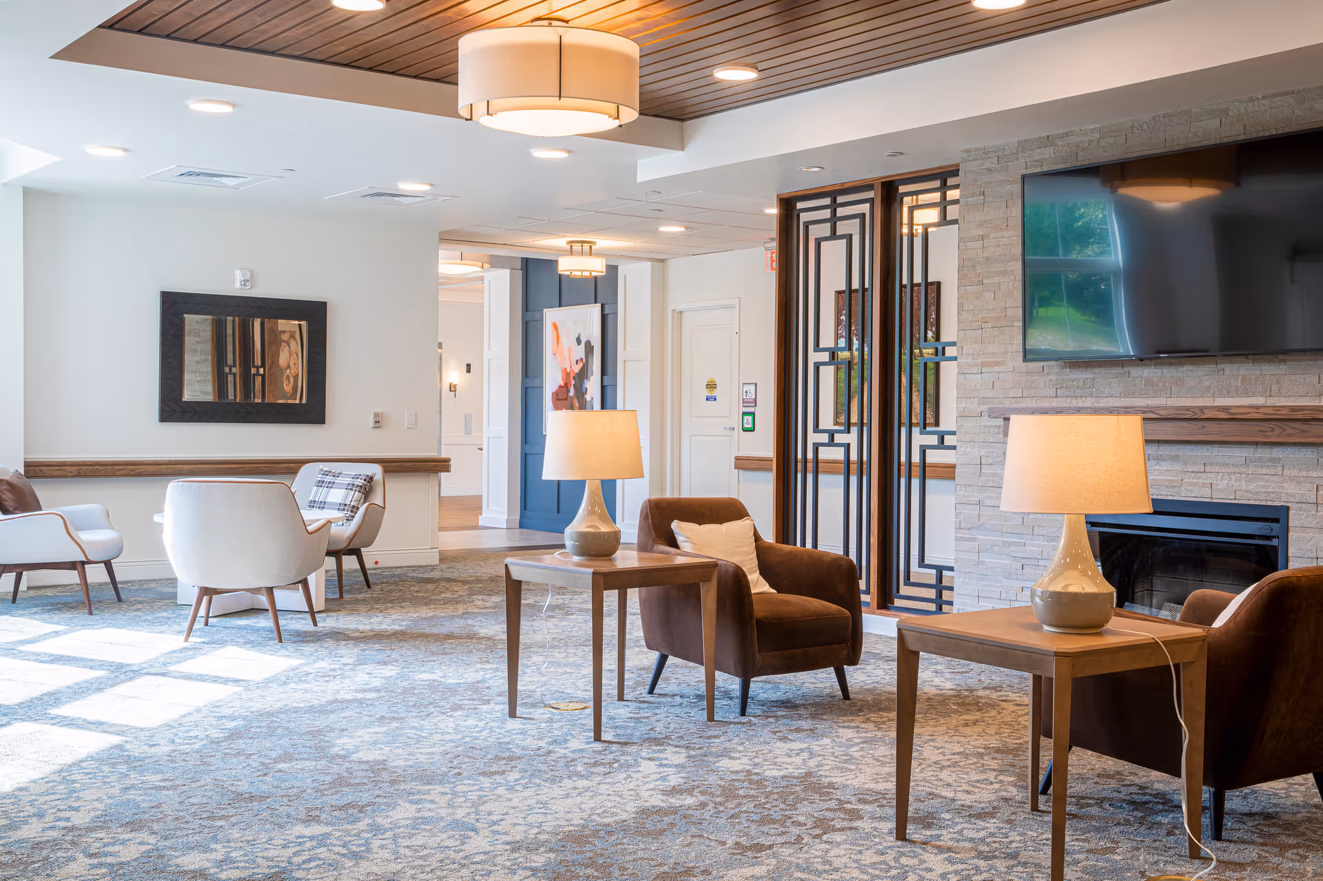 Bright, well-lit lounge with upholstered armchairs, side tables and lamps, a fireplace and wall-mounted TV.