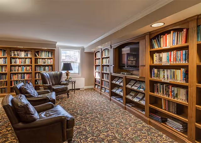 Cozy library-style sitting room with leather armchairs, built-in wooden bookshelves, a TV, and patterned carpet.