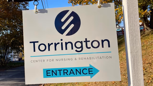 Outdoor sign reading 'Torrington Center for Nursing & Rehabilitation' with a blue arrow labeled 'Entrance.'