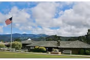 Exterior view of Del Mesa Carmel with flagpole, lawn, and distant mountains.