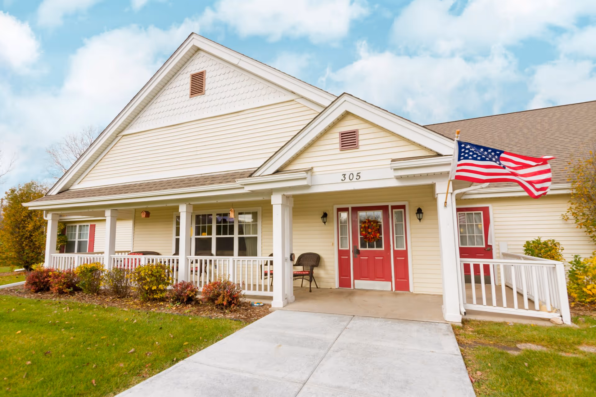 Senior living facility building with a covered porch, red doors, and an American flag.