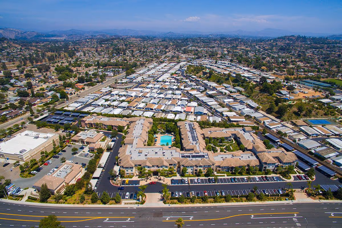Aerial view of the Woodland Village senior living complex with a central swimming pool, surrounding buildings, parking lots and neighboring residential area.