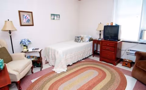 A Cardinal Care of Jacksonville bedroom with a bed, sofa, dresser, and TV.