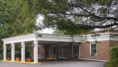 Exterior view of Beaver Valley Healthcare and Rehabilitation Center showing a brick building with a covered entrance supported by white columns, surrounded by trees and greenery.
