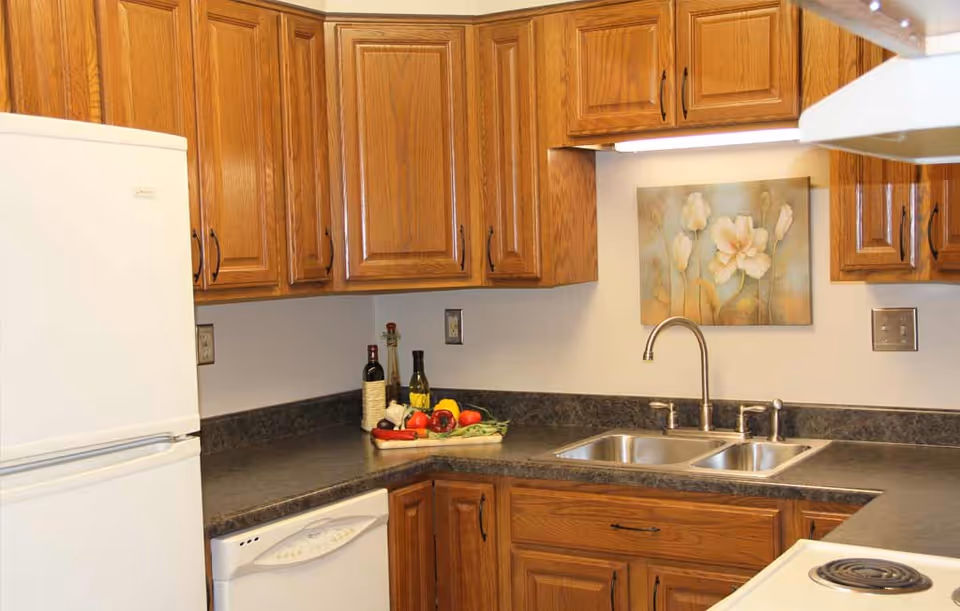 Kitchen with oak cabinets, a white refrigerator, double stainless sink, dark countertops, and a floral wall painting.