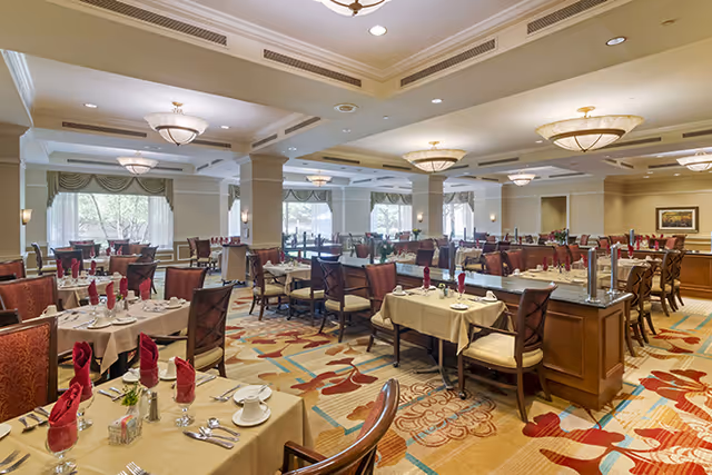 Spacious, well-lit dining room with multiple set tables, red napkins, chandeliers, and large windows.