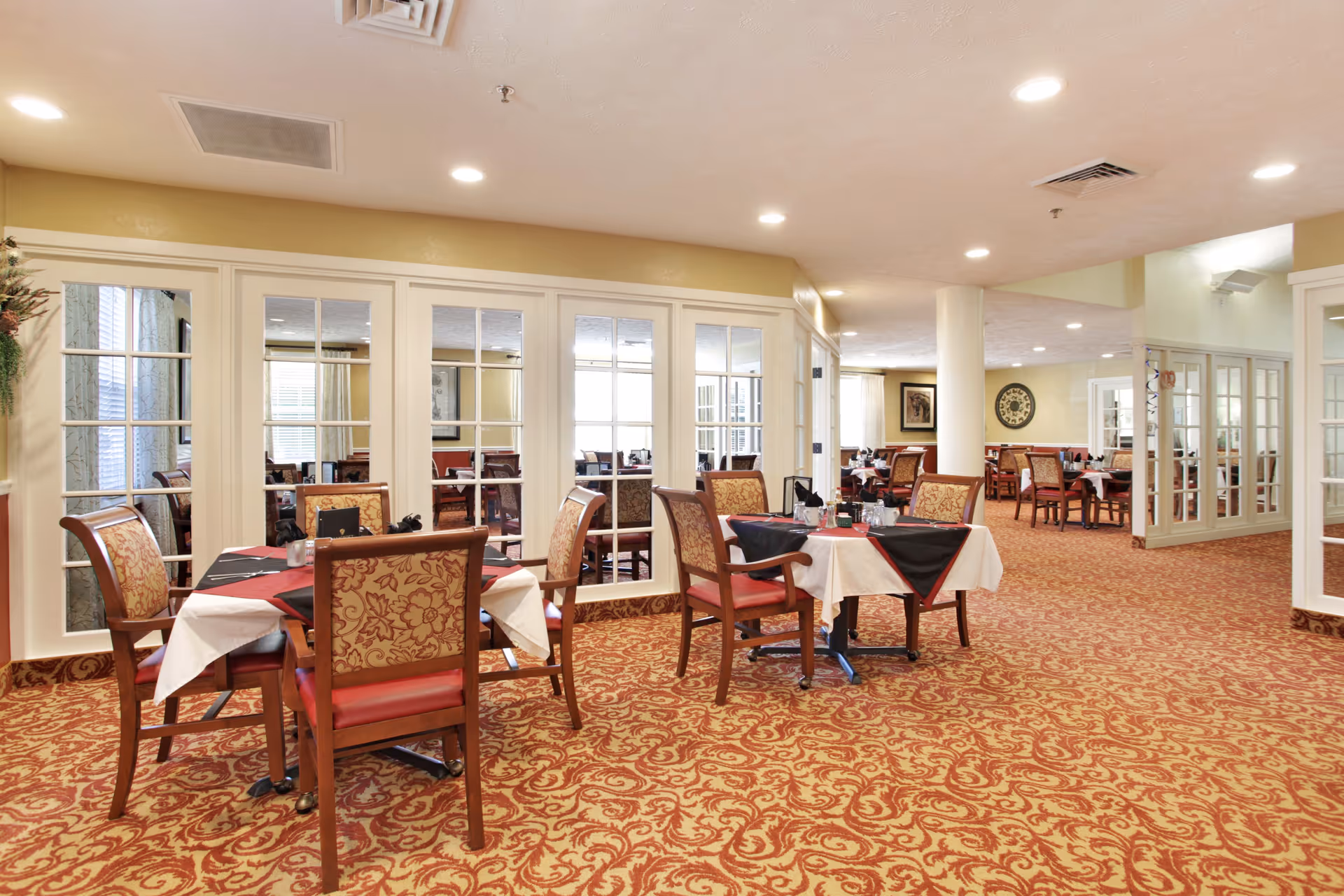 Well-lit dining room with multiple set tables, upholstered chairs, and a patterned carpet.