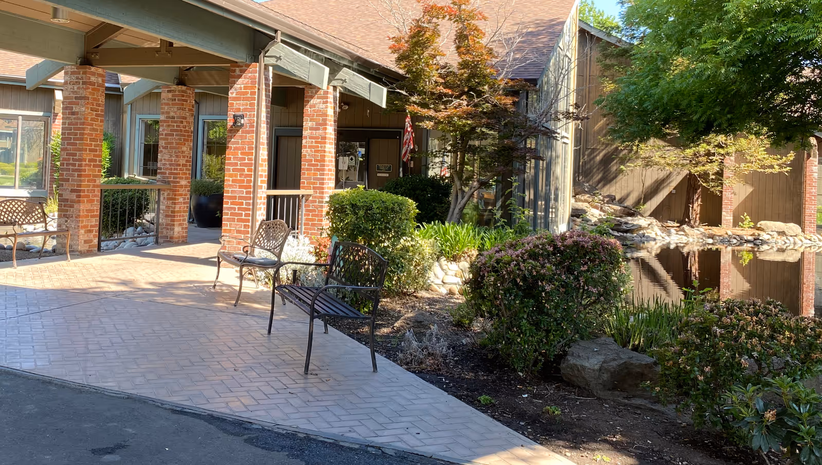 Covered building entrance with brick columns, metal benches, a landscaped pond and walkway.