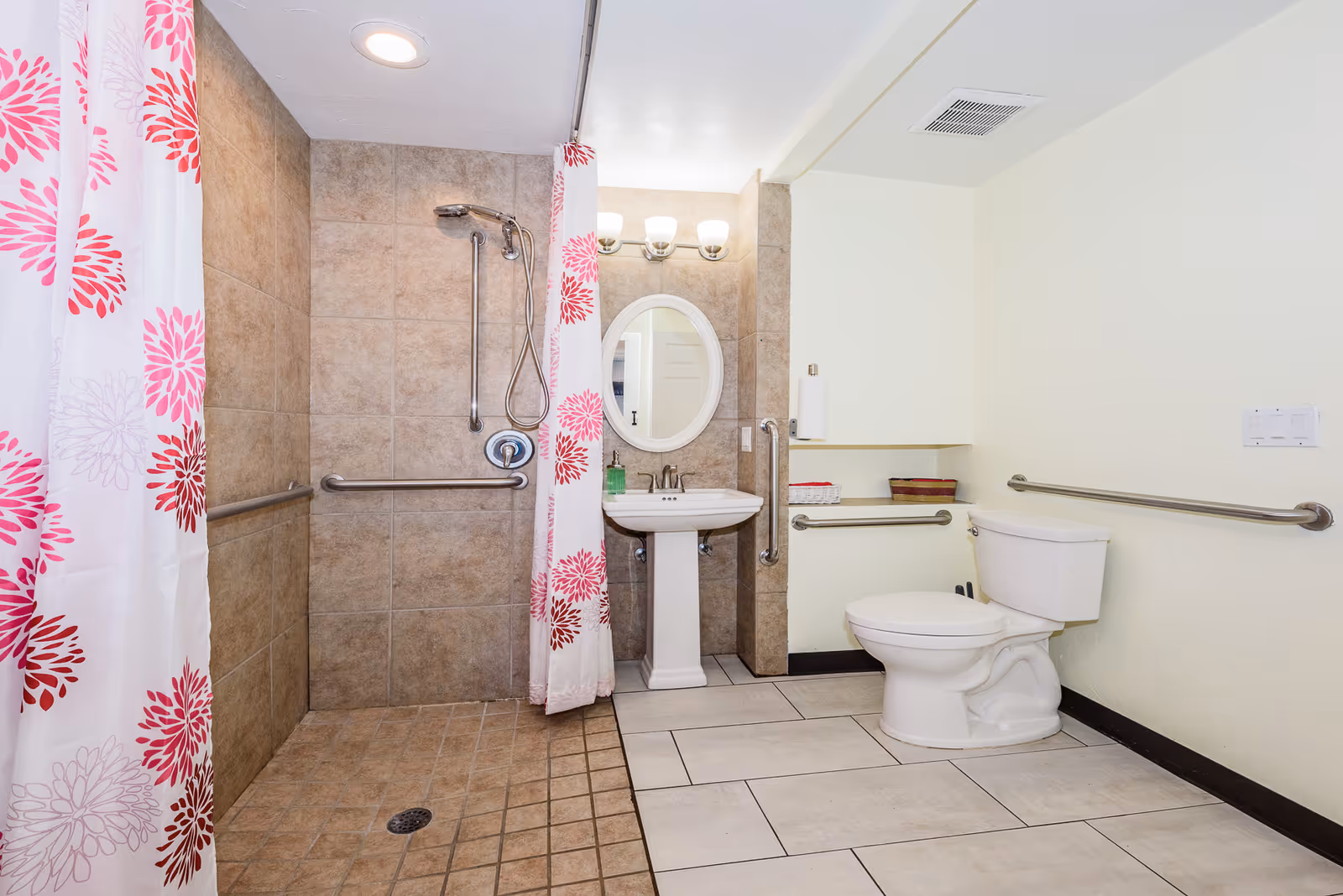 Accessible bathroom featuring a tiled walk-in shower with grab bars and pink floral shower curtains, a pedestal sink, and a toilet.