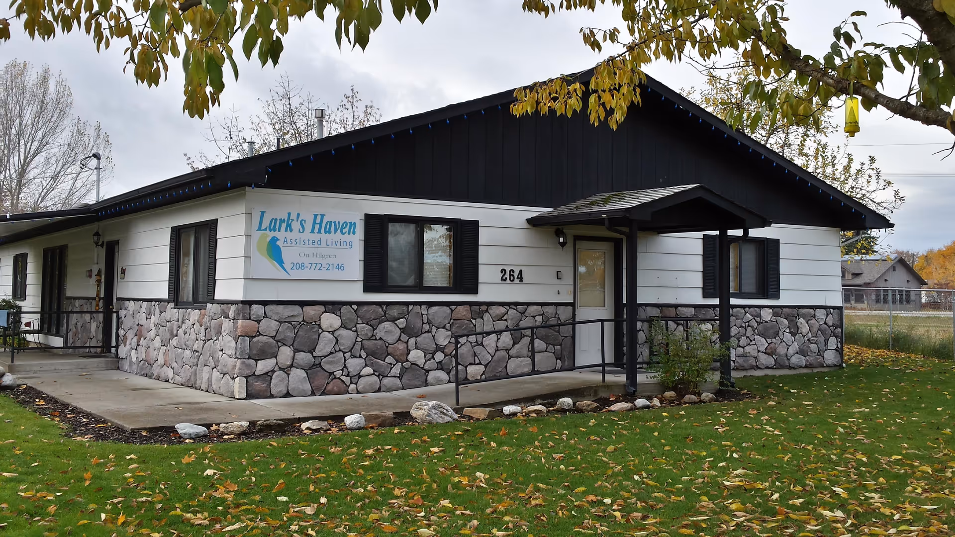 Single-story Lark's Haven Assisted Living building with a stone lower facade, sign and number 264, set on a grassy lawn under trees.
