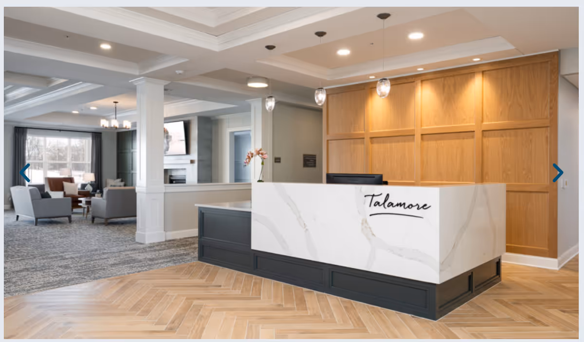 Modern reception desk with the word 'Talamore' in a bright senior living lobby showing seating and a fireplace in the background.