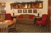 Cozy common room with a sofa flanked by red armchairs, side tables with lamps, a large mirror and framed art, and a round table with chairs.