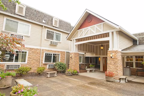 Exterior view of a senior living facility named Royalton Place featuring a covered entrance with stone pillars, benches, potted plants, and windows on the building facade.