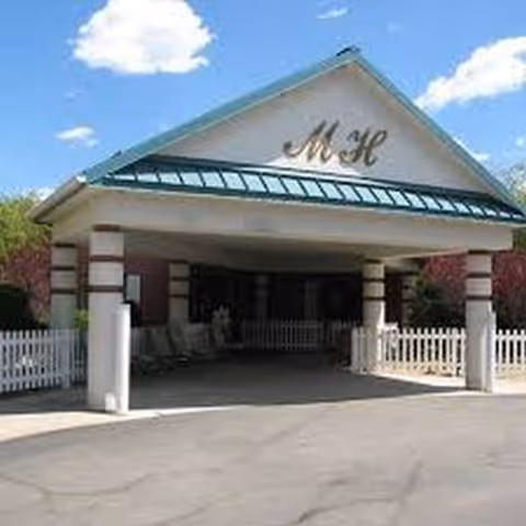 Front entrance of a senior living facility with porte-cochere and white fencing.