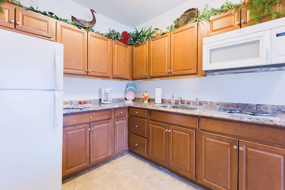 Bright kitchen with wooden cabinets, a white refrigerator and microwave, marble-look countertops, sink and small appliances.