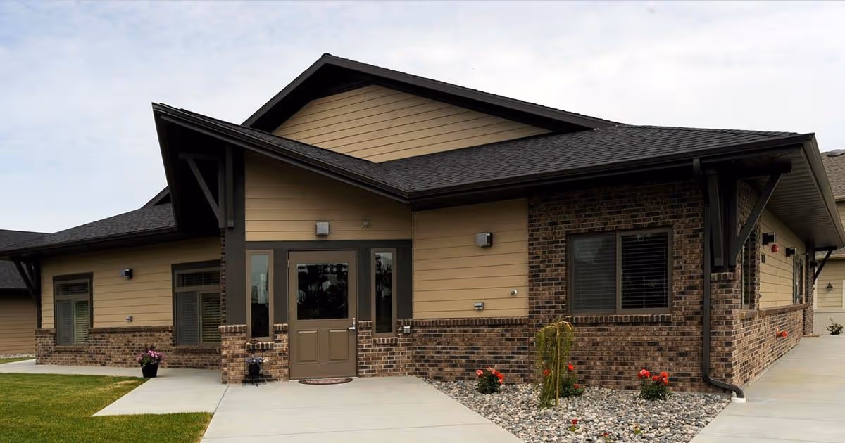 Front exterior of a single-story brick and siding cottage with an entrance door, walkway, and small landscaped rock garden.