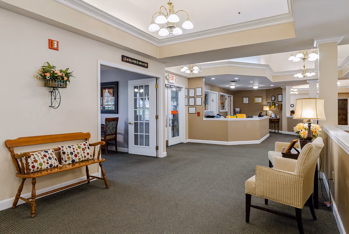 Spacious senior living facility lobby with seating, a reception desk, and overhead chandeliers.