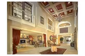 Spacious and elegant interior of a senior living facility with high ceilings, large windows, chandeliers, and a central table with a floral arrangement. The area includes seating spaces and decorative elements, creating a welcoming and comfortable atmosphere.
