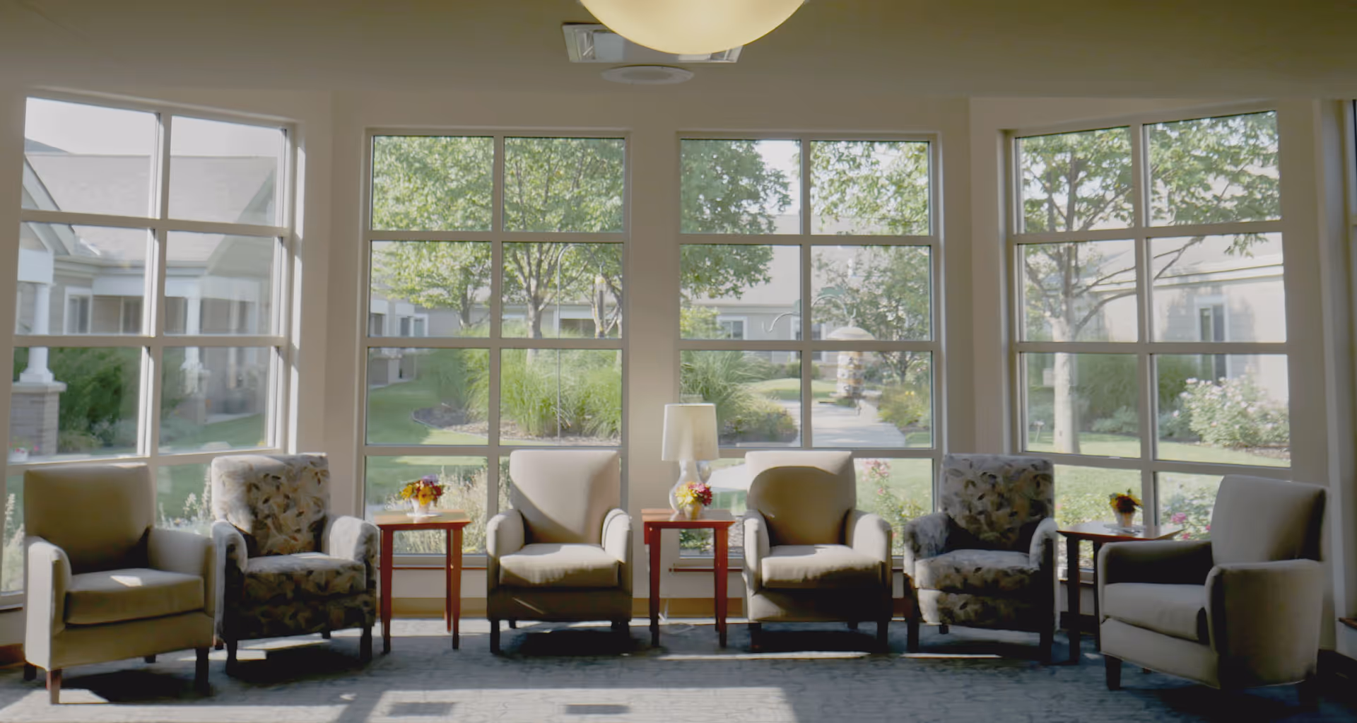Sunlit seating area with six armchairs and side tables arranged in front of large windows overlooking a landscaped courtyard.
