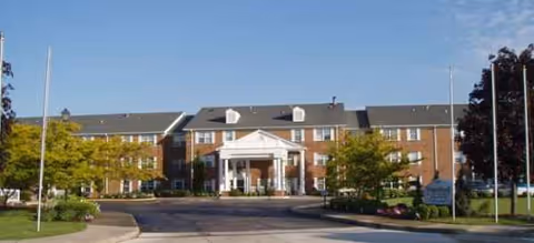Brick senior living facility with a central covered entrance and manicured landscaping.