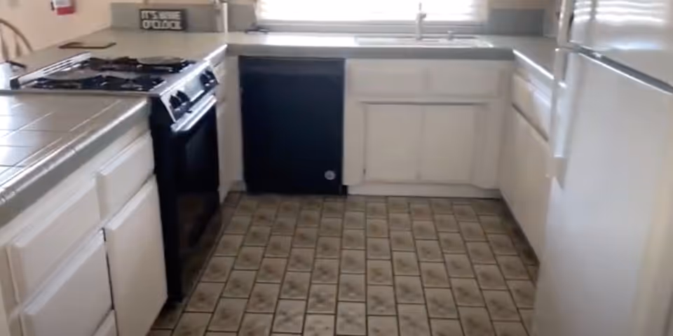 Small kitchen with white cabinets, tiled floor, a gas stove, dishwasher and a sink beneath a window.