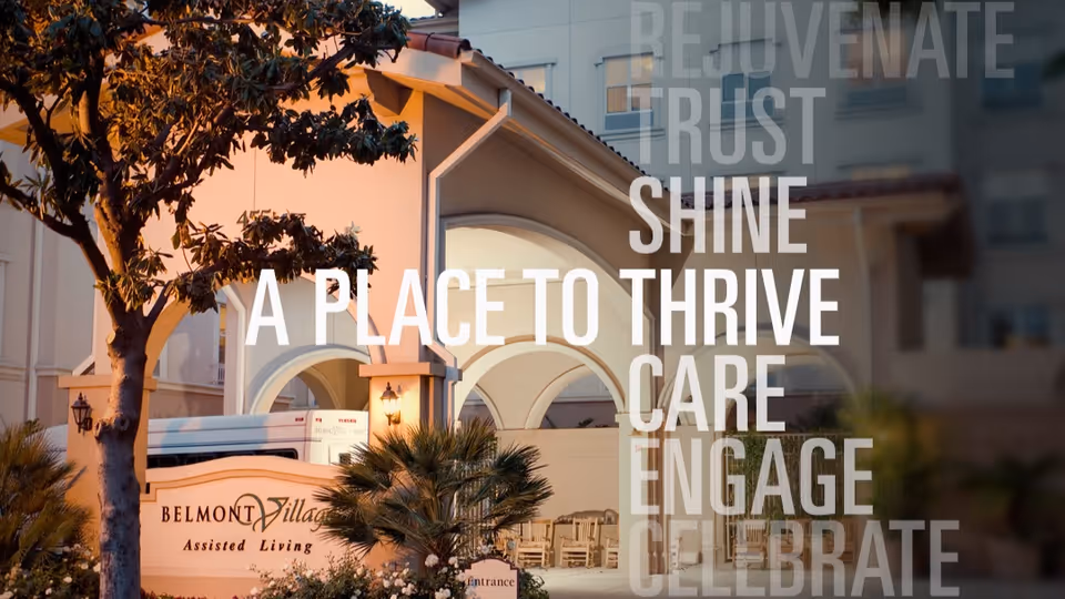 Exterior view of Belmont Village Assisted Living building with arched entrance, palm trees, and a tree in the foreground during sunset. Words overlay the image including 'REJUVENATE', 'TRUST', 'SHINE', 'A PLACE TO THRIVE', 'CARE', 'ENGAGE', and 'CELEBRATE'.