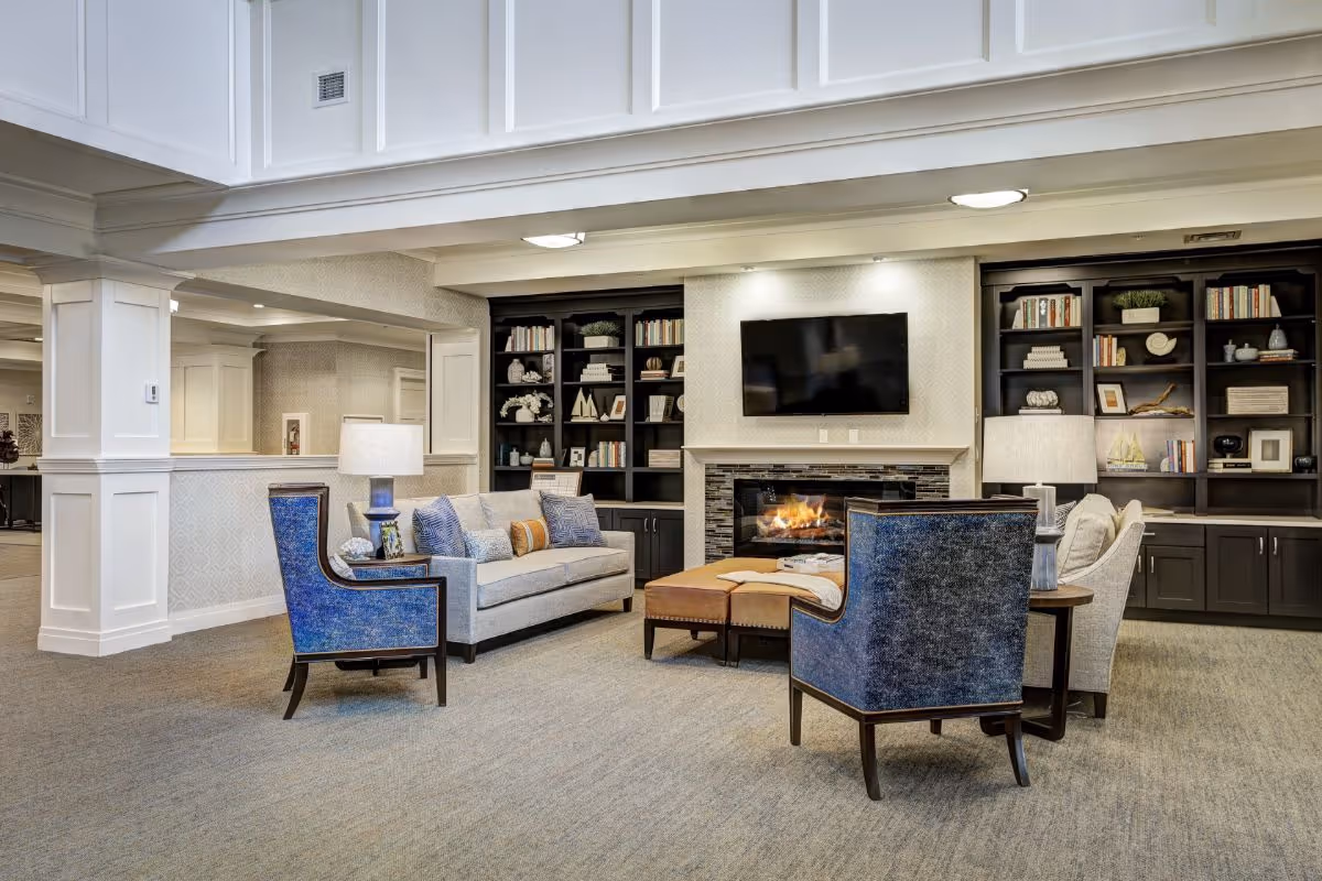 Comfortable seating area with a sofa and armchairs arranged around a fireplace and wall-mounted TV, flanked by built-in bookshelves.