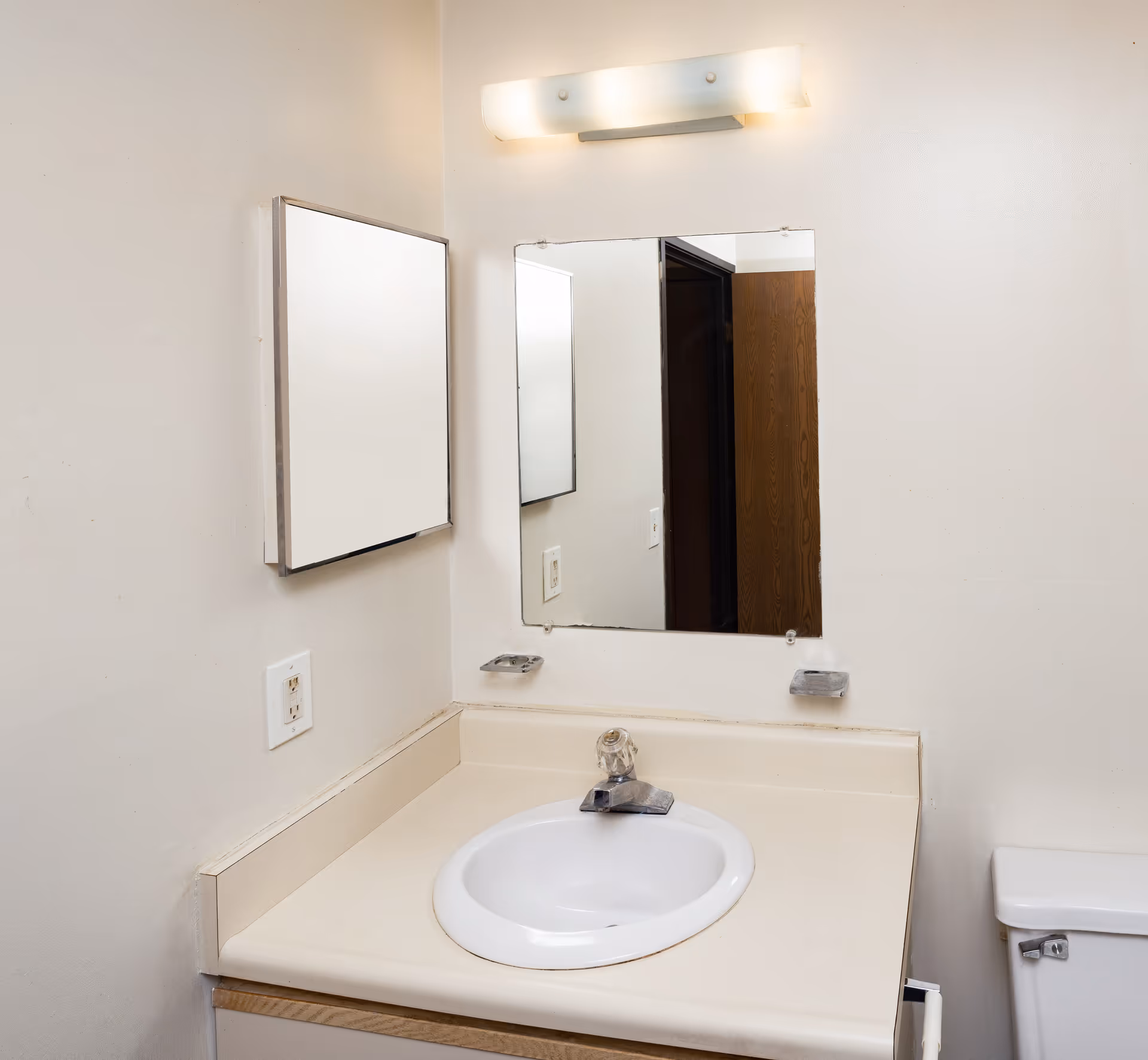 A small bathroom vanity with a sink, wall-mounted mirror and medicine cabinet, light fixture, and a partial view of a toilet.