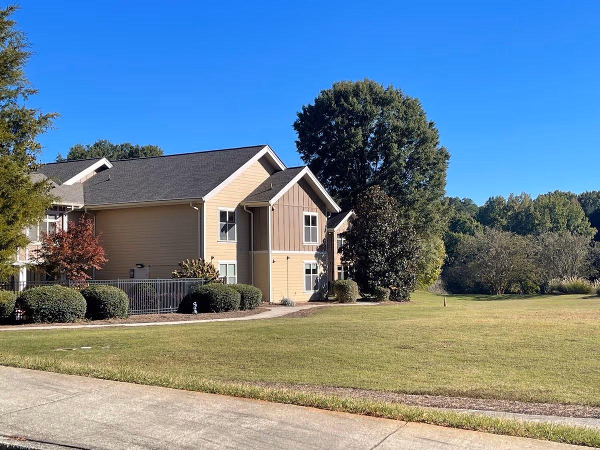 Two-story beige residential building with shrubs and a large mowed lawn under a clear blue sky.