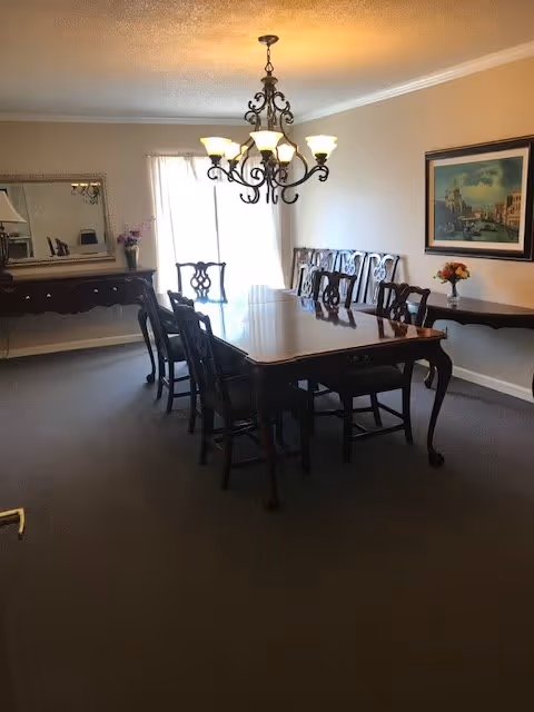 A formal dining room featuring a long wooden table with chairs beneath an ornate chandelier, with a sideboard, mirror, and framed painting.