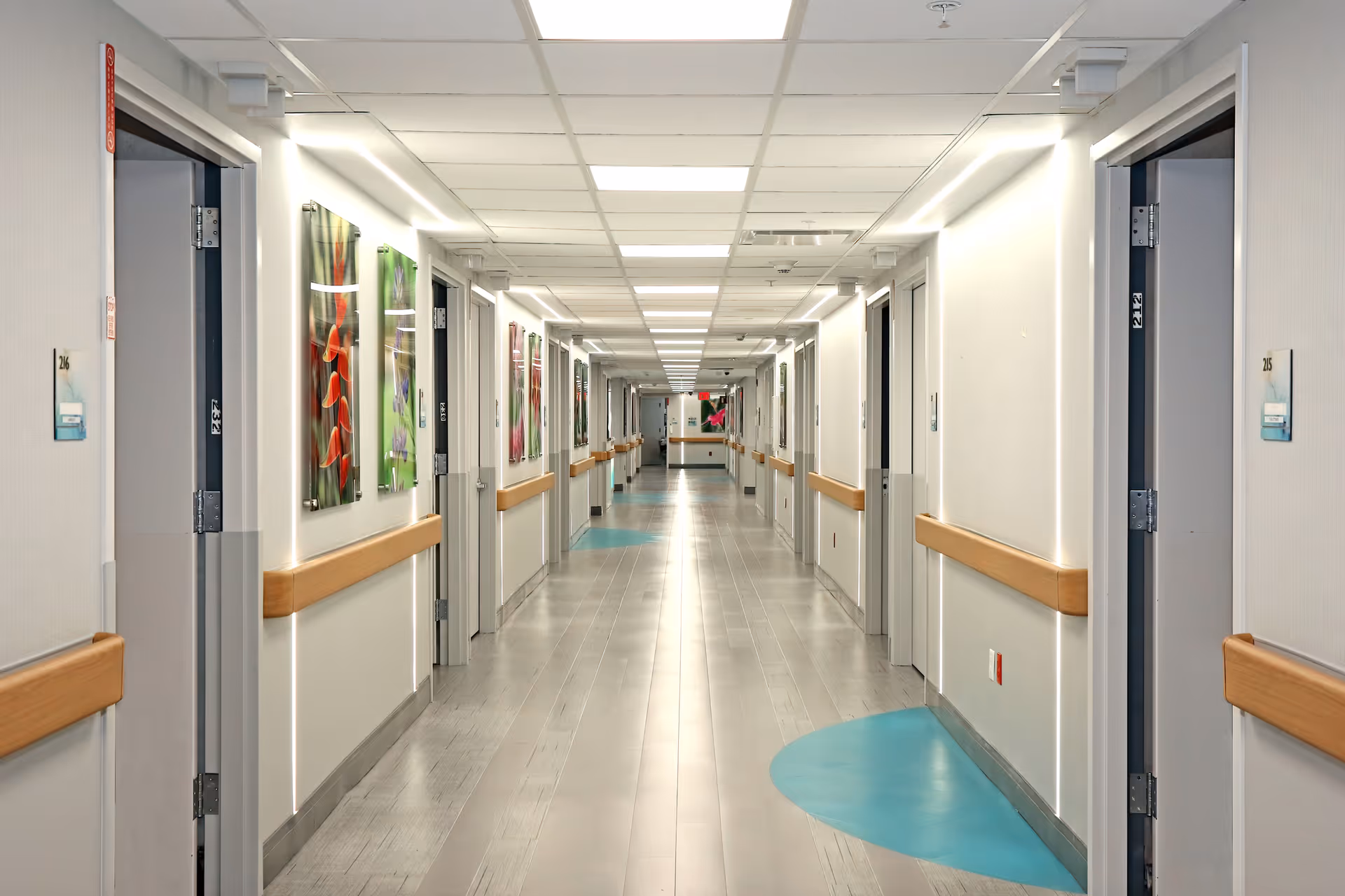 Long, well-lit interior hallway of a nursing and rehabilitation center with doors, handrails, and artwork along the walls.