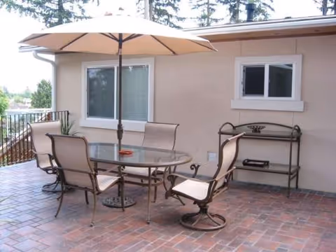 Outdoor brick patio with glass table, chairs, and umbrella beside a beige building.