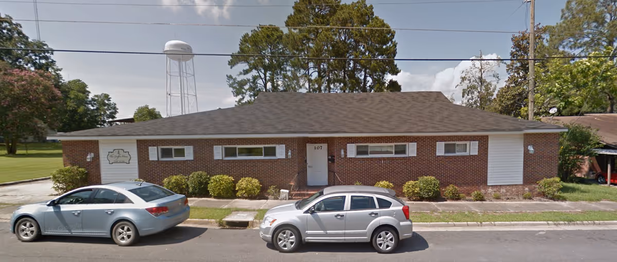 Brick senior living building with parked cars and a small front yard