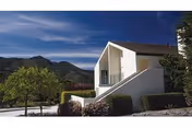 White stucco building with exterior stairs, landscaped shrubs and trees, and hills under a deep blue sky.
